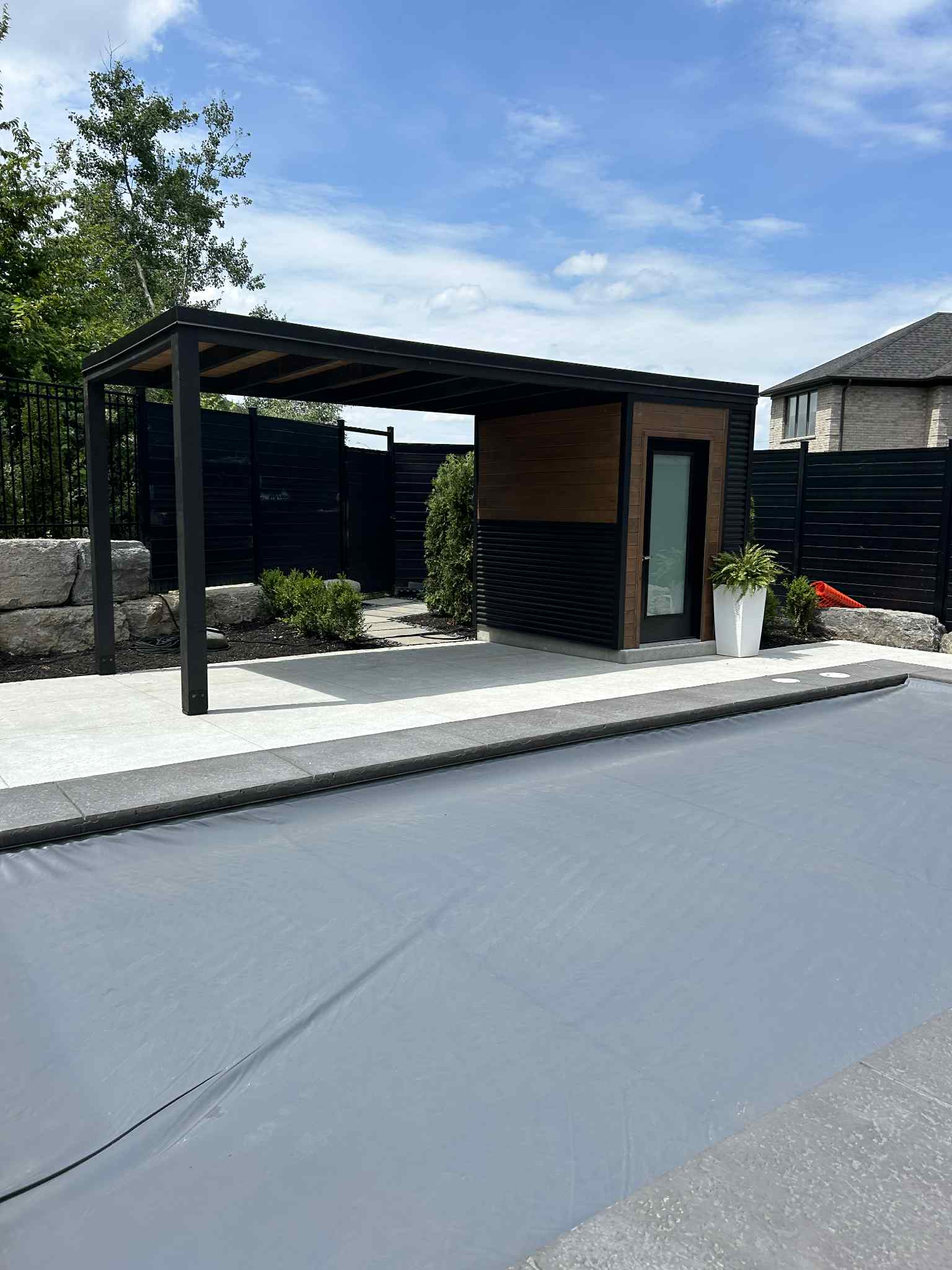Modern black and wood-look poolside pavilion and storage structure in Komoka